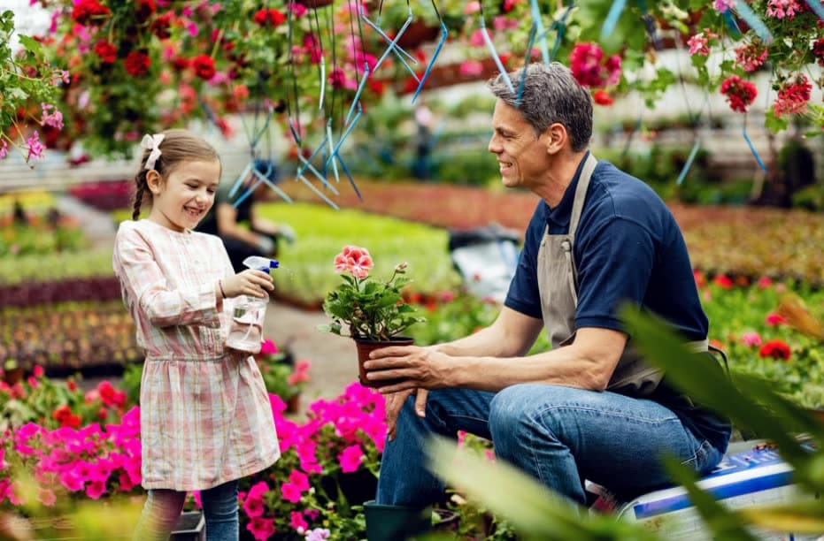 A grower showing a young girl a potted plant in a greenhouse