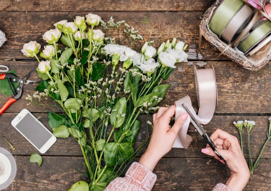 Hands arranging white flowers and eucalyptus on a wooden table