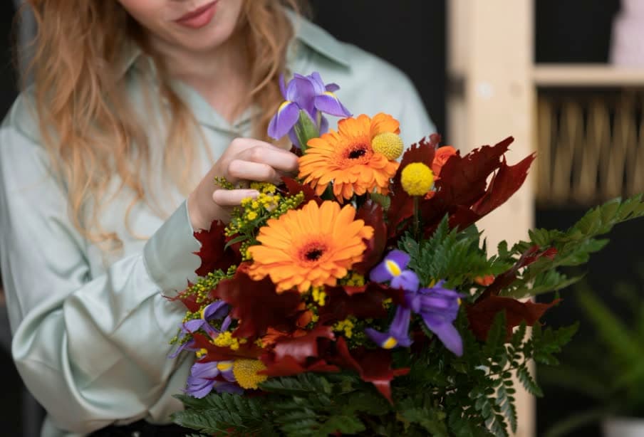 A florist arranging orange gerberas and purple flowers