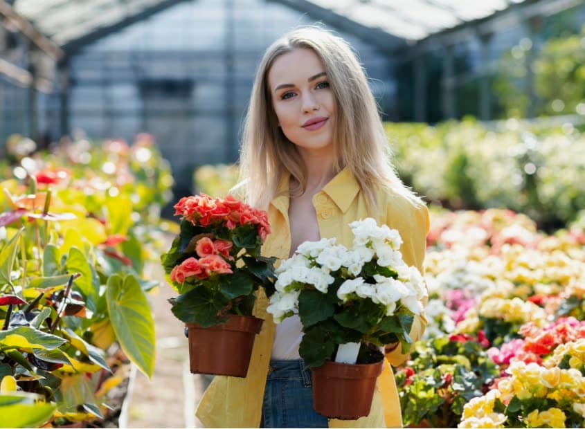 A grower in a yellow jacket holding potted flowers