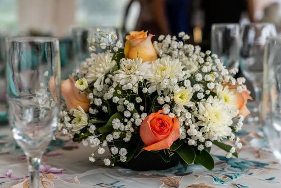 A low centrepiece of white and peach roses among wine glasses